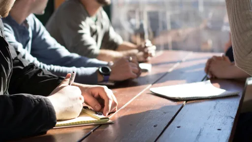 People around a table, writing notes on a notepad