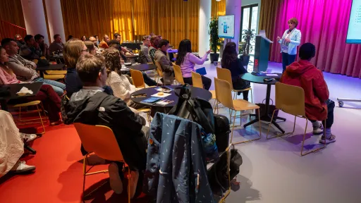 a woman is presenting in front of a room full of people.