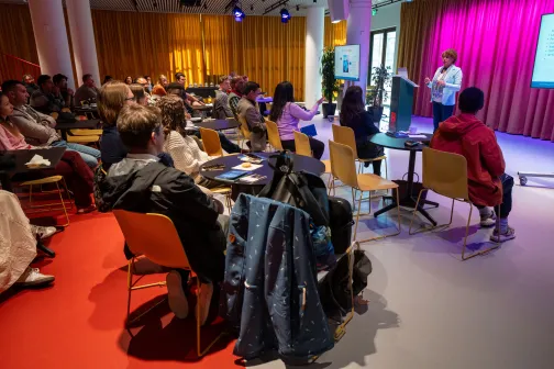 a woman is presenting in front of a room full of people.