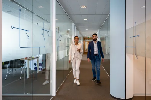 Two young employees walk down the hallway of the Security Delta (HSD) office