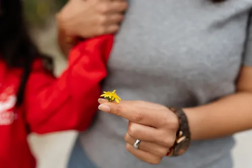 A shot focused on the yellow flower that a woman is holding in her hand.