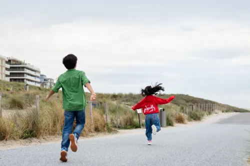 Two kids skipping and jumping playfully on a street next to a dune.